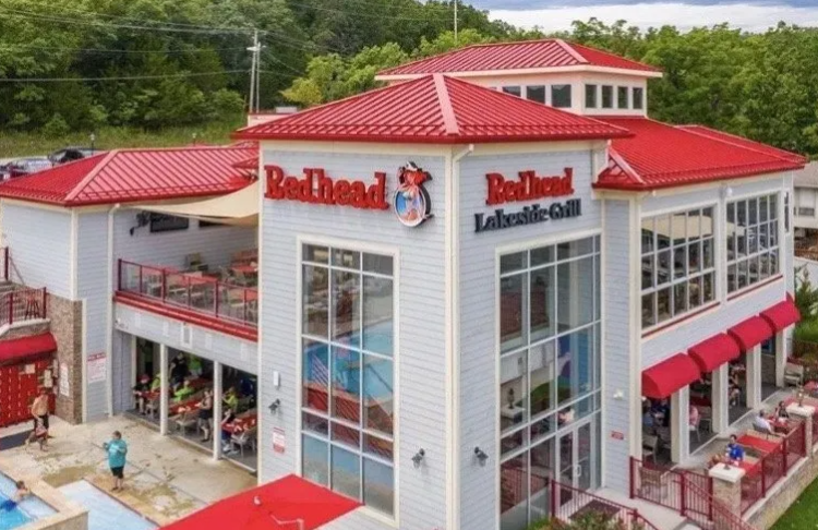 Aerial view of RedHead restaurant with red roofs and white exterior, set among trees.