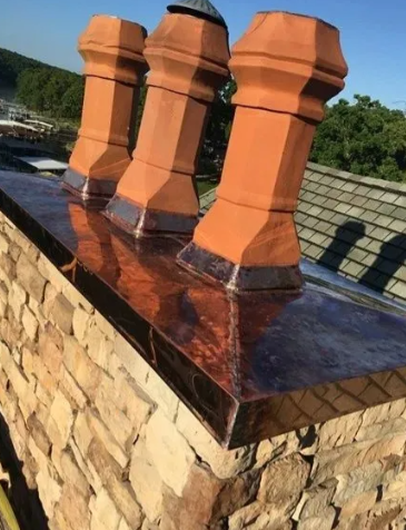 Three terracotta chimney vents on a glossy dark roof above a stone wall in sunlight