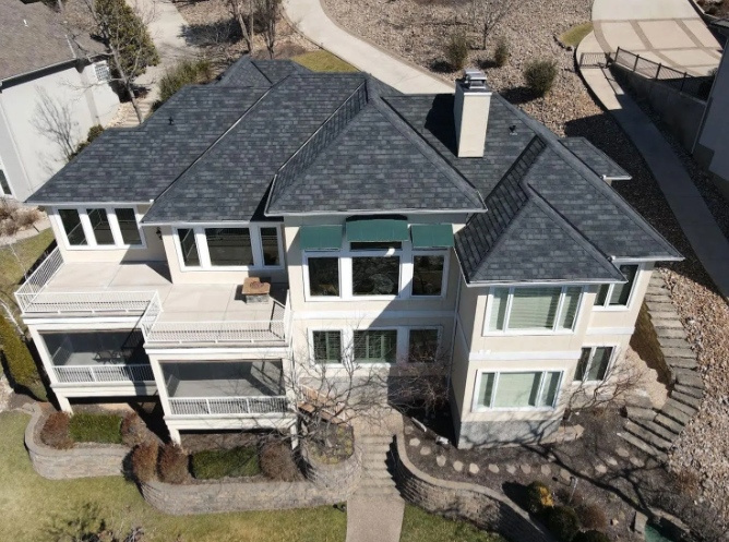 Aerial view of a large two-story house with gray roofs, white siding, and a stone retaining wall.