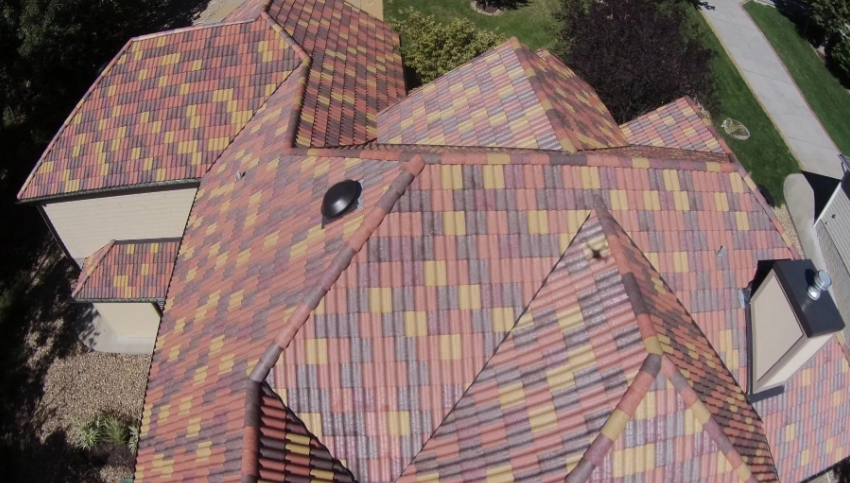 Aerial view of a roof with multicolored shingles and a small skylight, surrounded by trees.