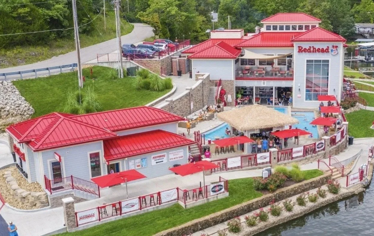 Red-roofed waterfront restaurant complex with outdoor seating and a dock by the water