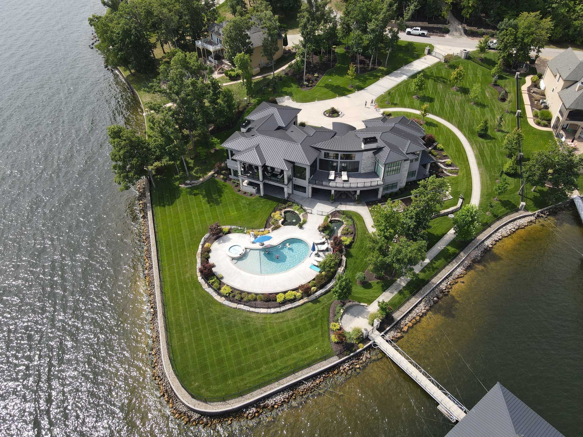Aerial view of a lakeside house with a pool, landscaped lawn, and dock beside the water.