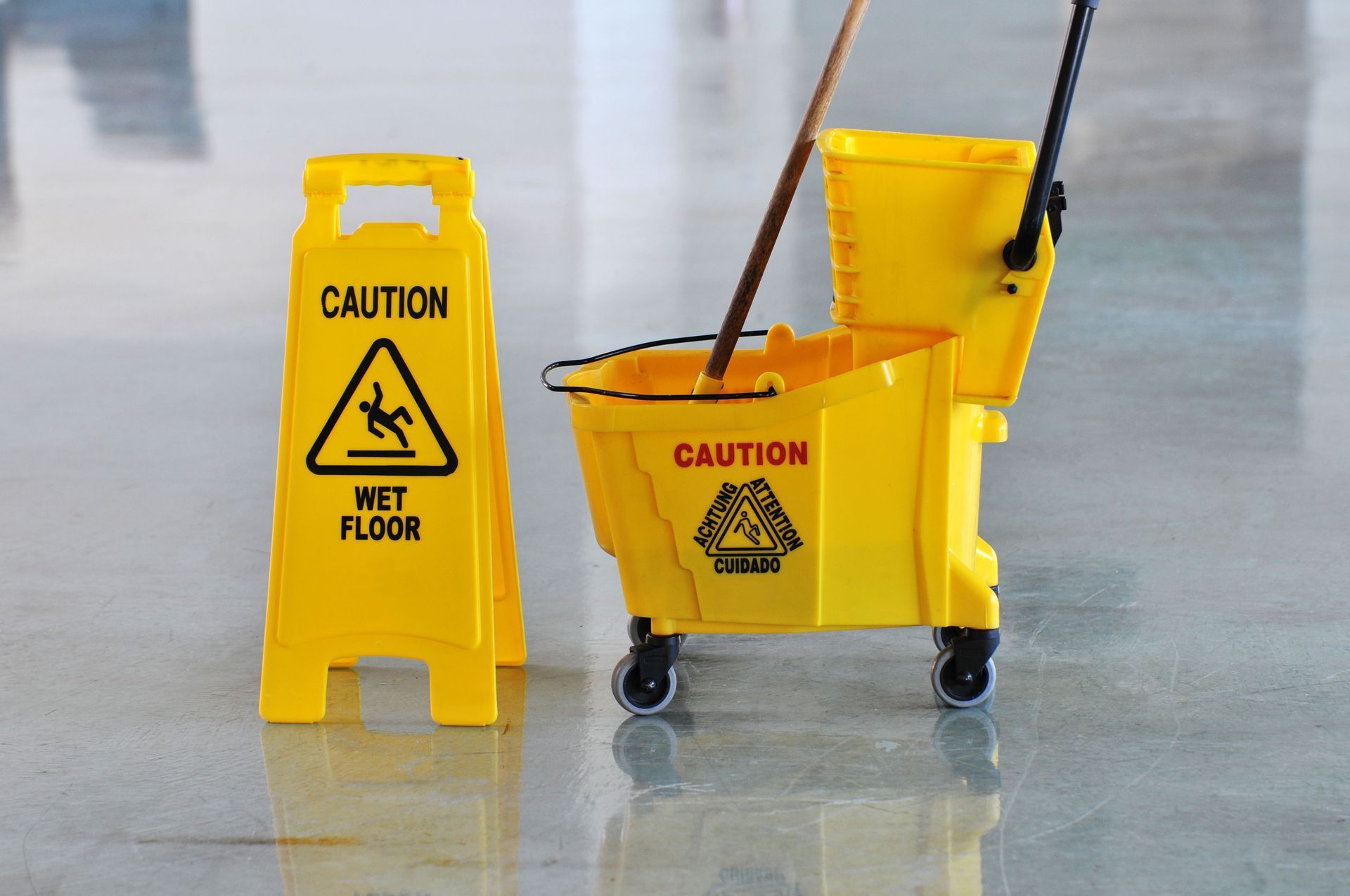 Yellow wet floor sign and cleaning cart with mop, on shiny floor.