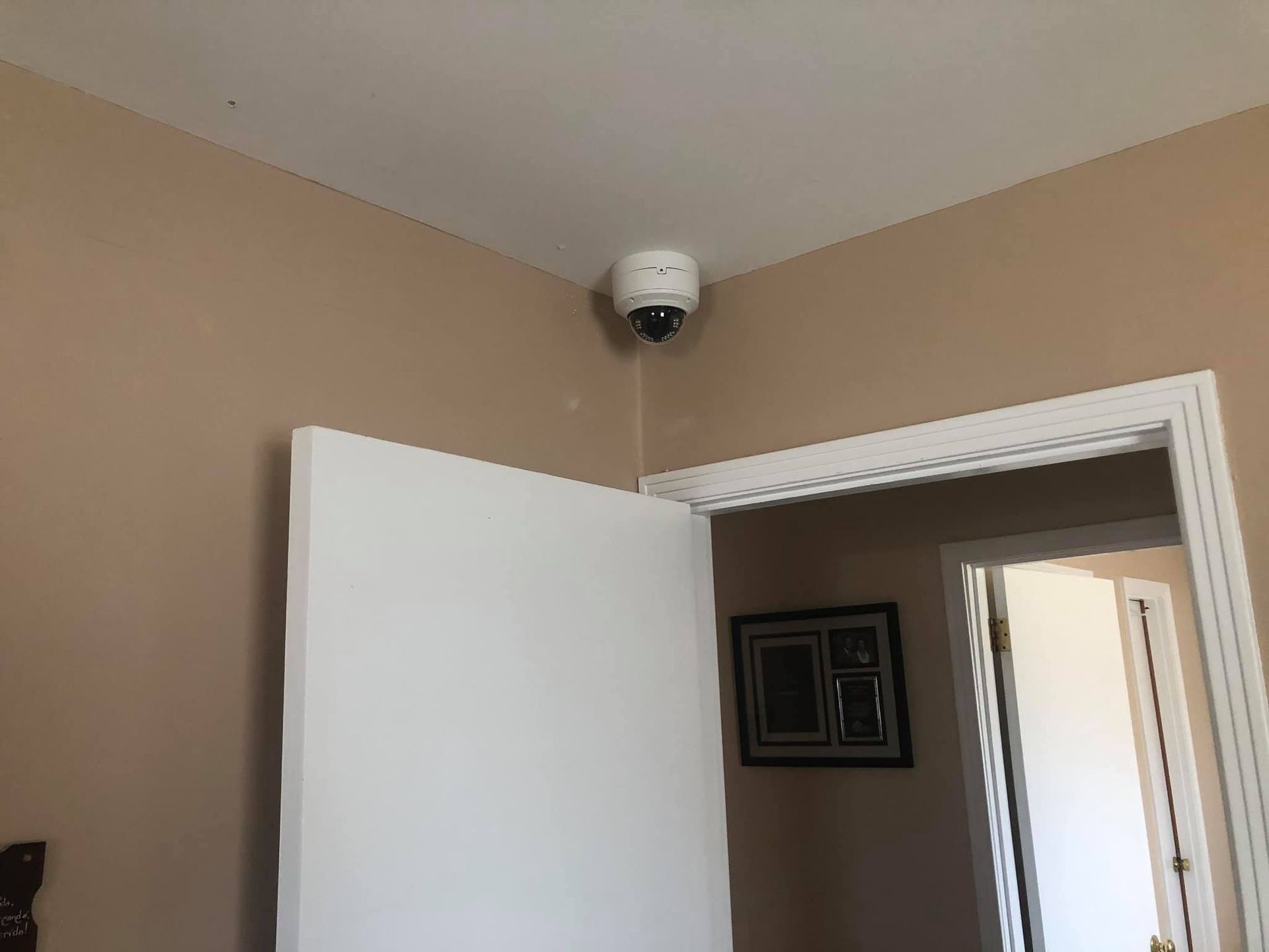A security camera is mounted on the ceiling above a door in a room.
