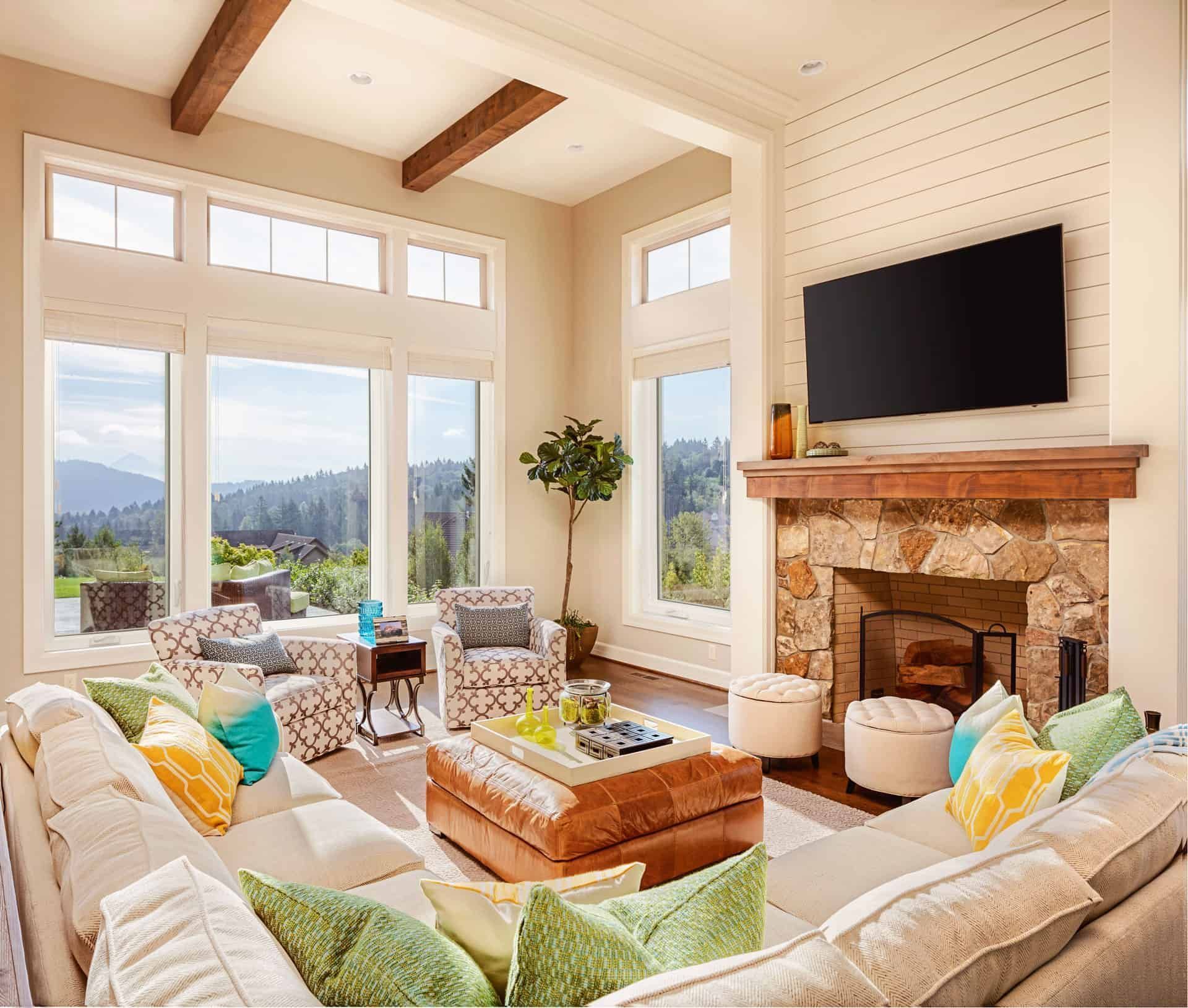 Living room with large windows, a stone fireplace, and a sectional sofa with colorful pillows.