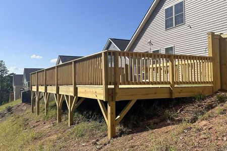 A large wooden deck is sitting on top of a grassy hill in front of a house.