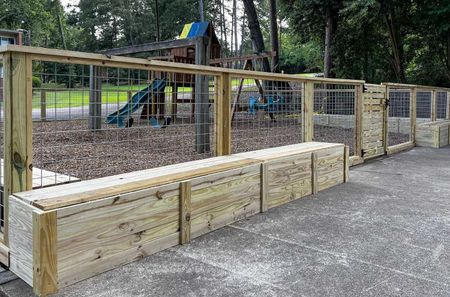 A wooden fence with a bench in front of a playground.