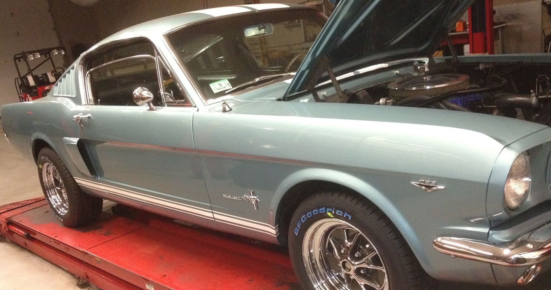 A blue mustang is parked on a red ramp with the hood open.