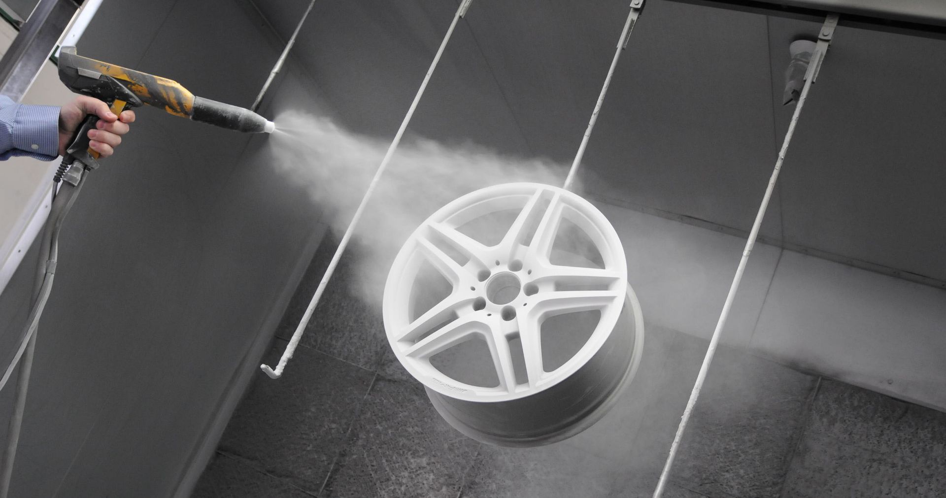 A person is spraying powder paint on a white wheel.