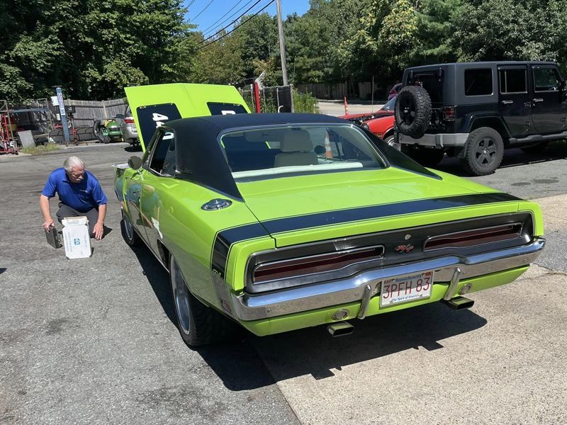 A man is kneeling next to a green dodge charger.