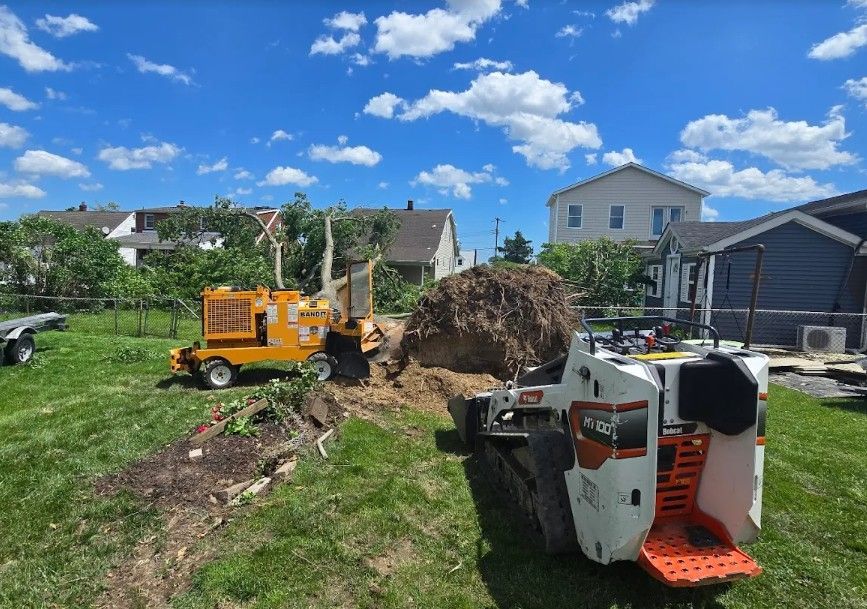 Construction equipment moving dirt in a residential yard under a blue sky, with houses in the background.