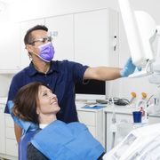 A man wearing a purple mask is standing next to a woman in a dental chair