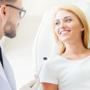 A woman is smiling while sitting in a chair talking to a dentist.