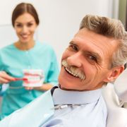 A man with a mustache is smiling while sitting in a dental chair