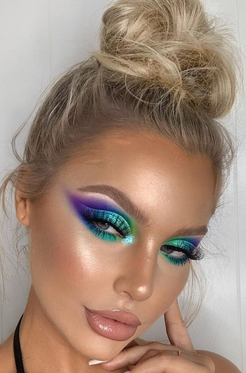 a close up of a woman 's face with colorful eye makeup and a bun .