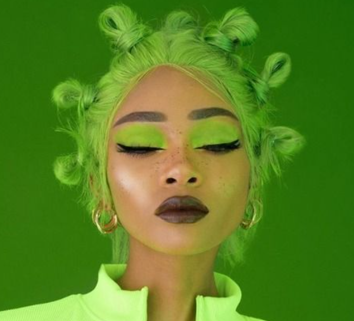 a woman with green hair and green makeup is wearing a neon green jacket .