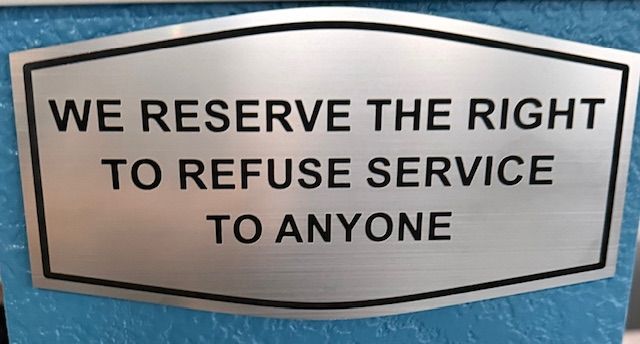 A silver sign on a blue surface that reads: WE RESERVE THE RIGHT TO REFUSE SERVICE TO ANYONE.
