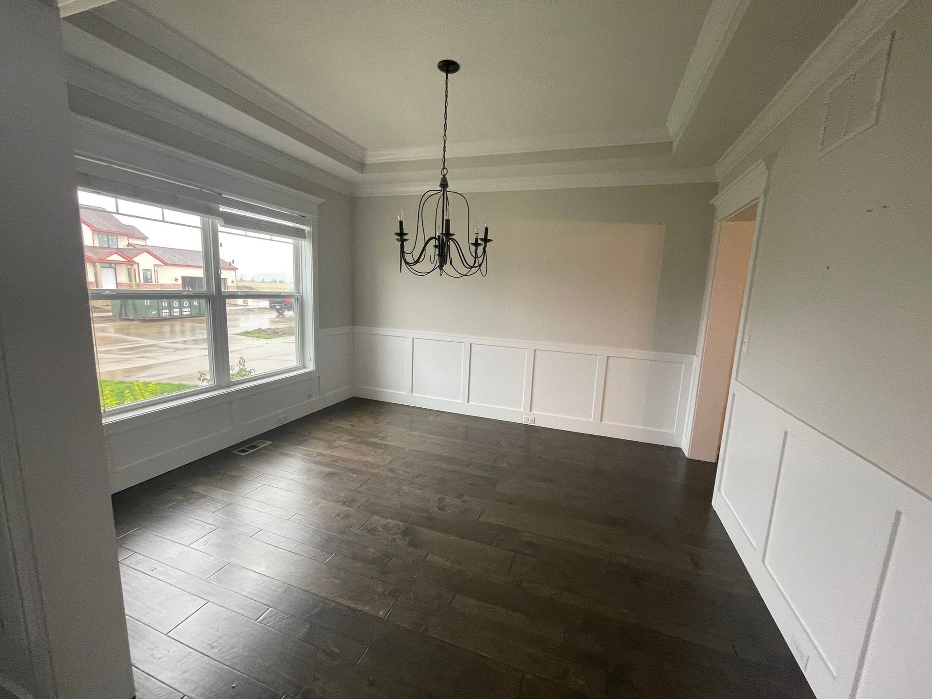 An empty dining room with hardwood floors and a chandelier hanging from the ceiling.