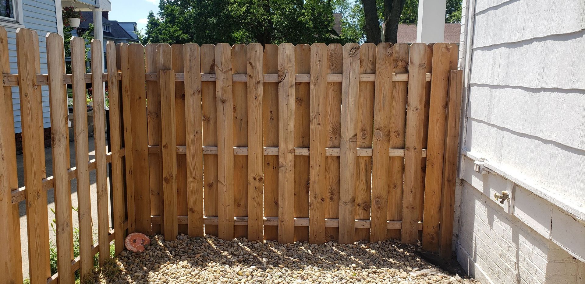 A wooden fence is surrounding a gravel area in front of a house.