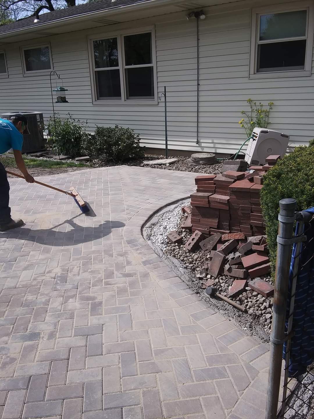 A man is sweeping a brick walkway in front of a house.