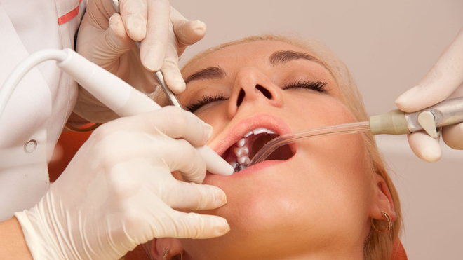 Woman at dentist, mouth open, receiving dental cleaning. Dentist holding tools.