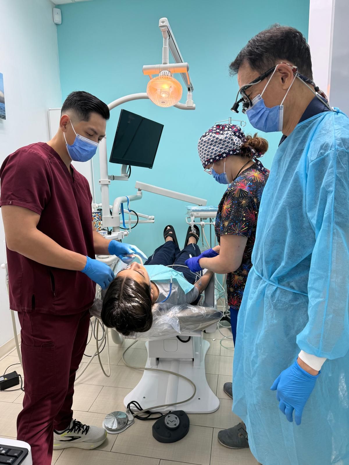Dentist and assistants in a dental office examining a patient in a chair under a light.