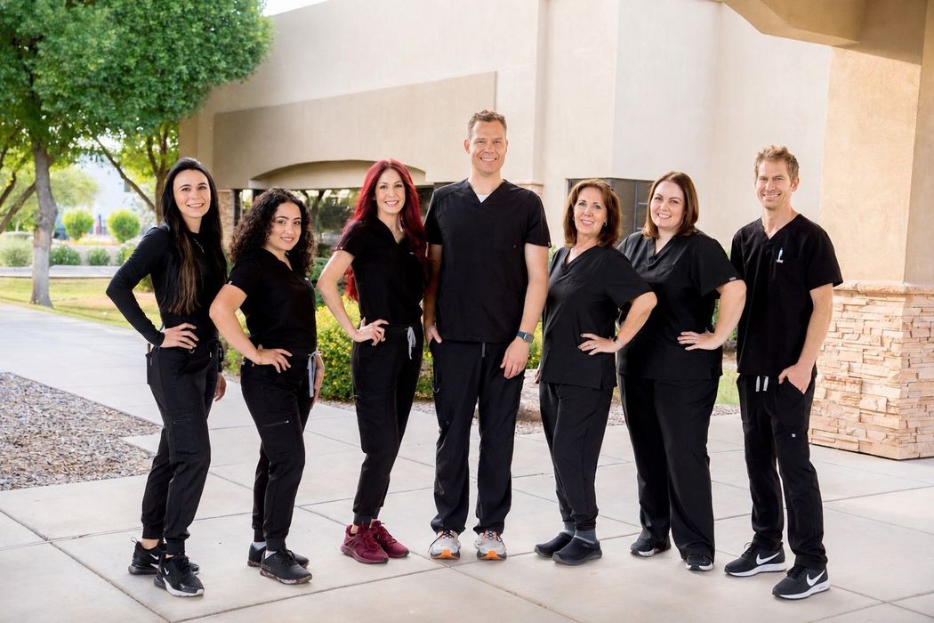 Group of seven people in black outfits posing outdoors beside a building.