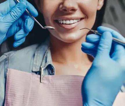 Gloved hands holding dental tools near a smiling patient in a bib