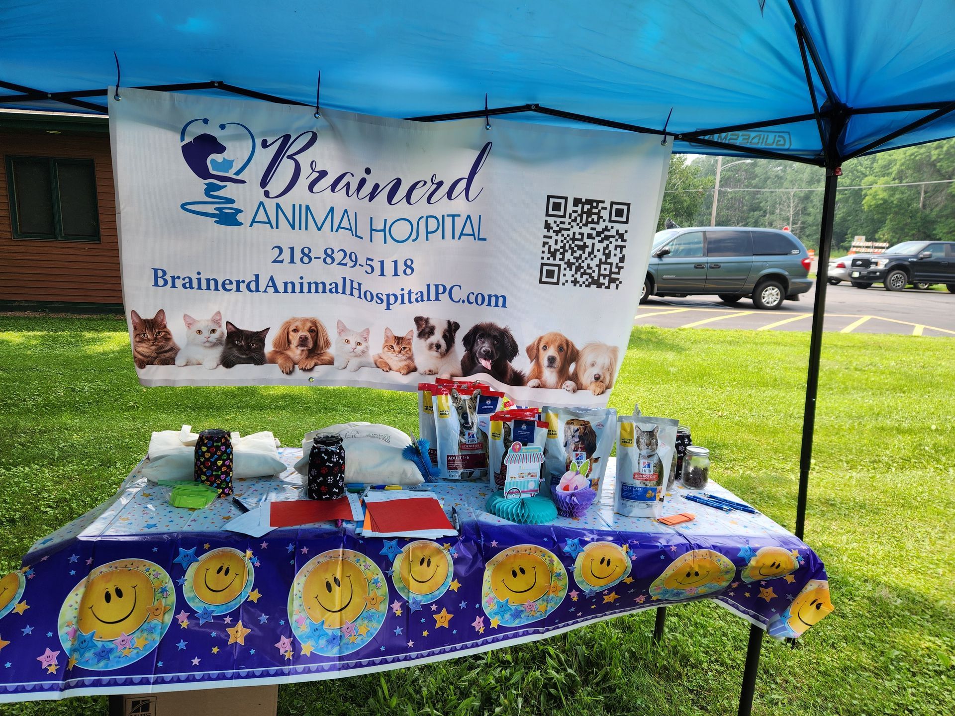 Brainerd Animal Hospital booth at an outdoor event, displaying pet products and a banner with images of pets.