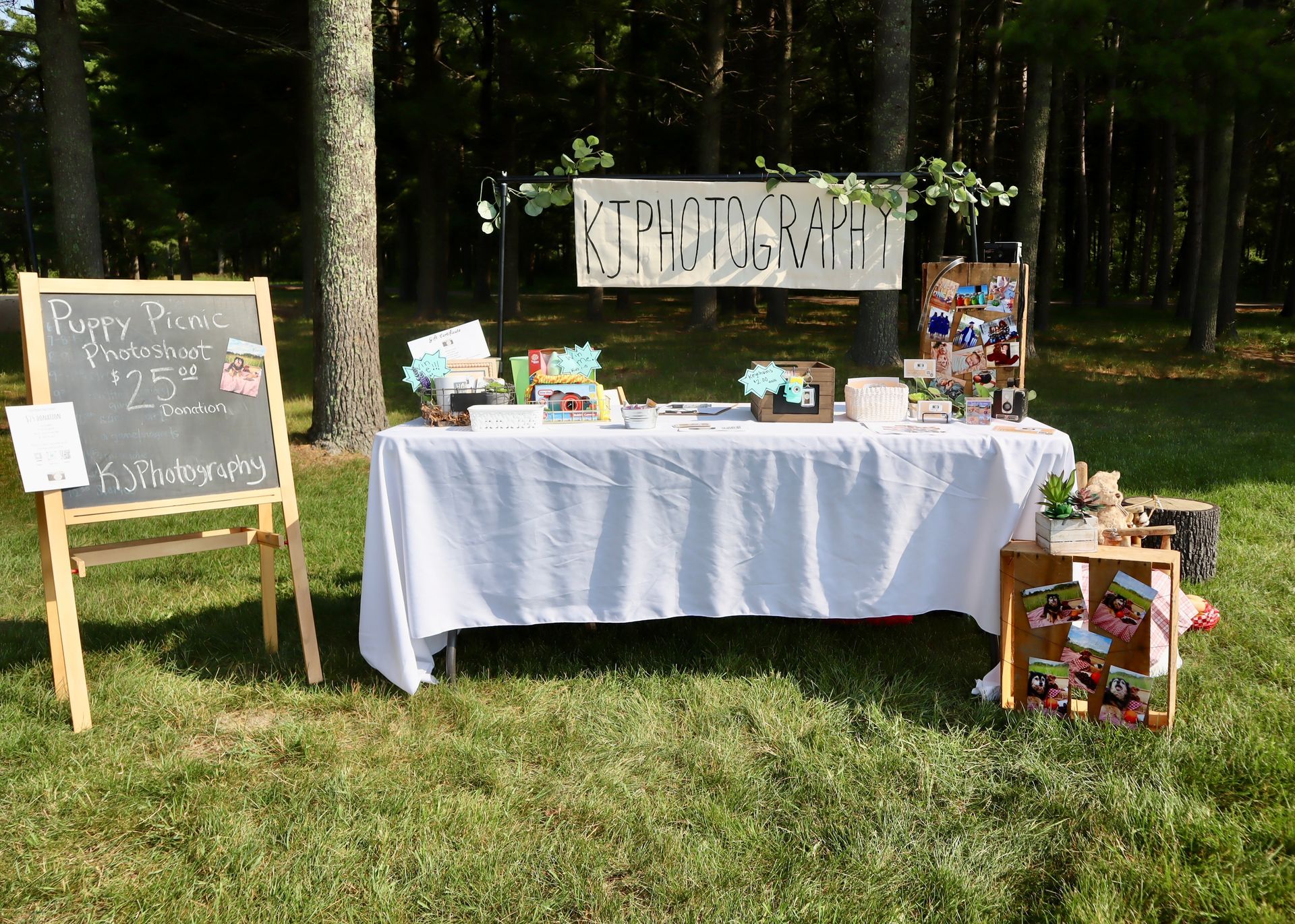 A table with a white table cloth is sitting in the grass next to a chalkboard.