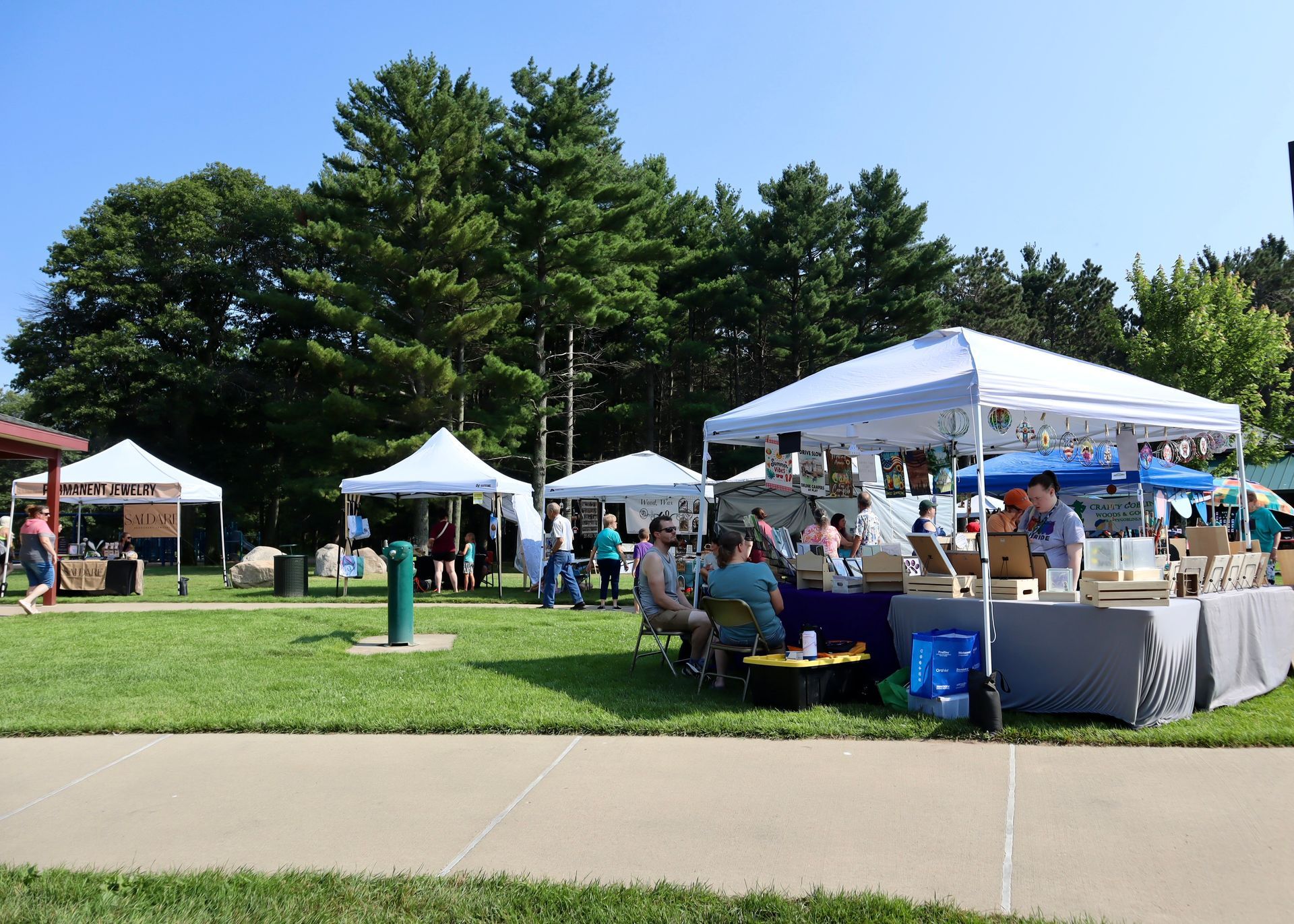 A group of people are gathered under tents in a park.