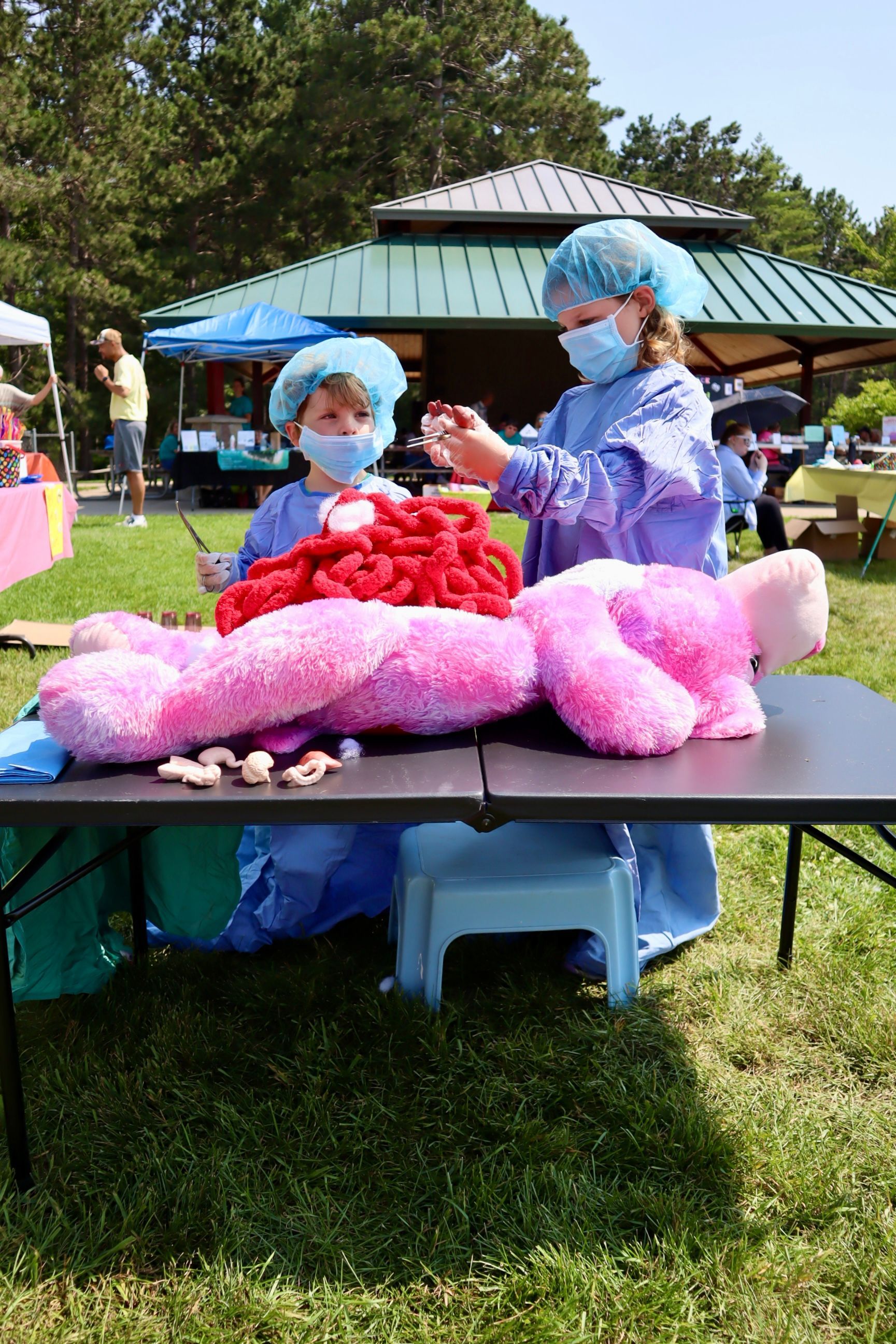 Two people are sitting at a table with a pink teddy bear on it.