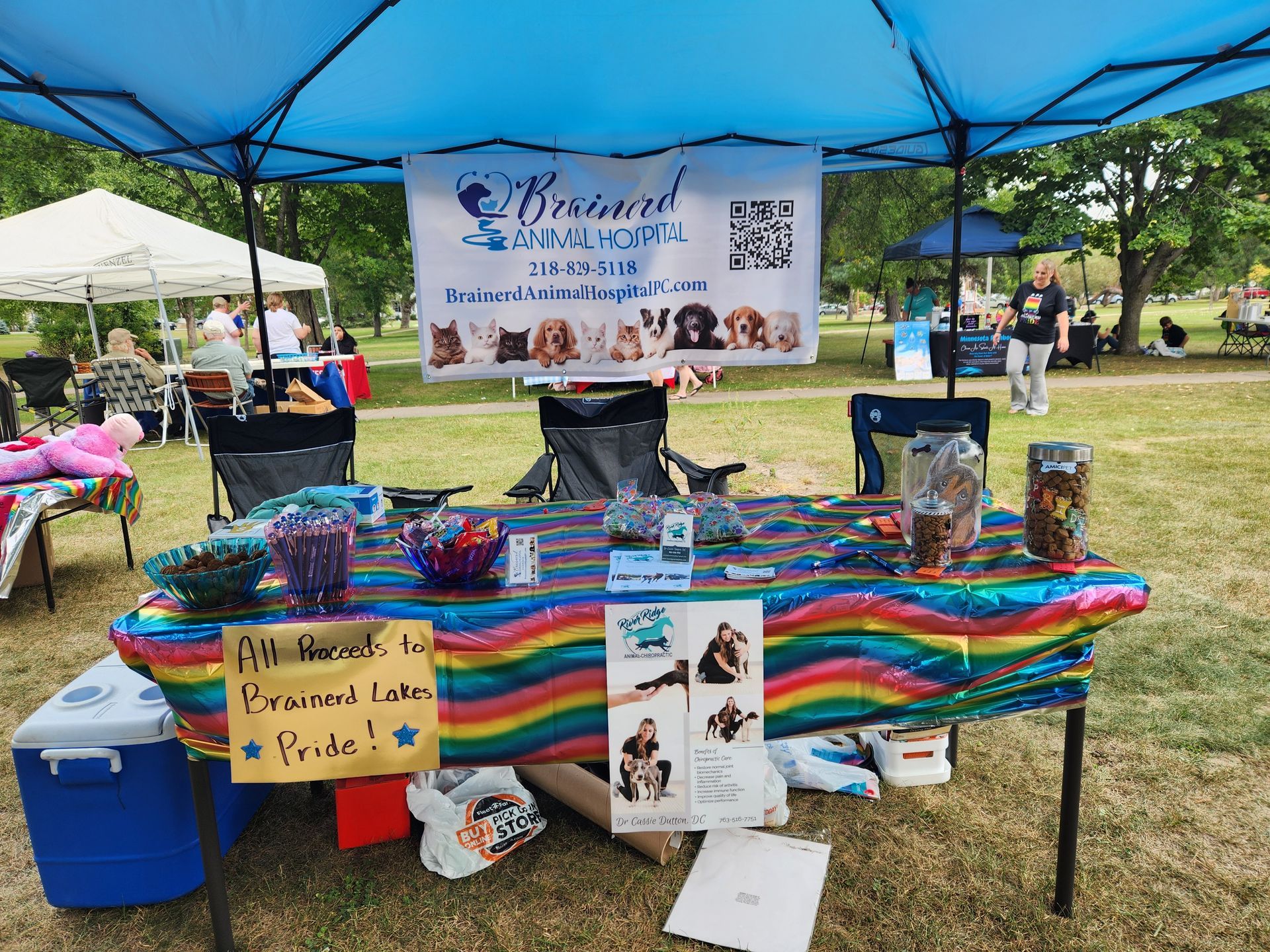 A table with a rainbow tablecloth is under a blue tent.