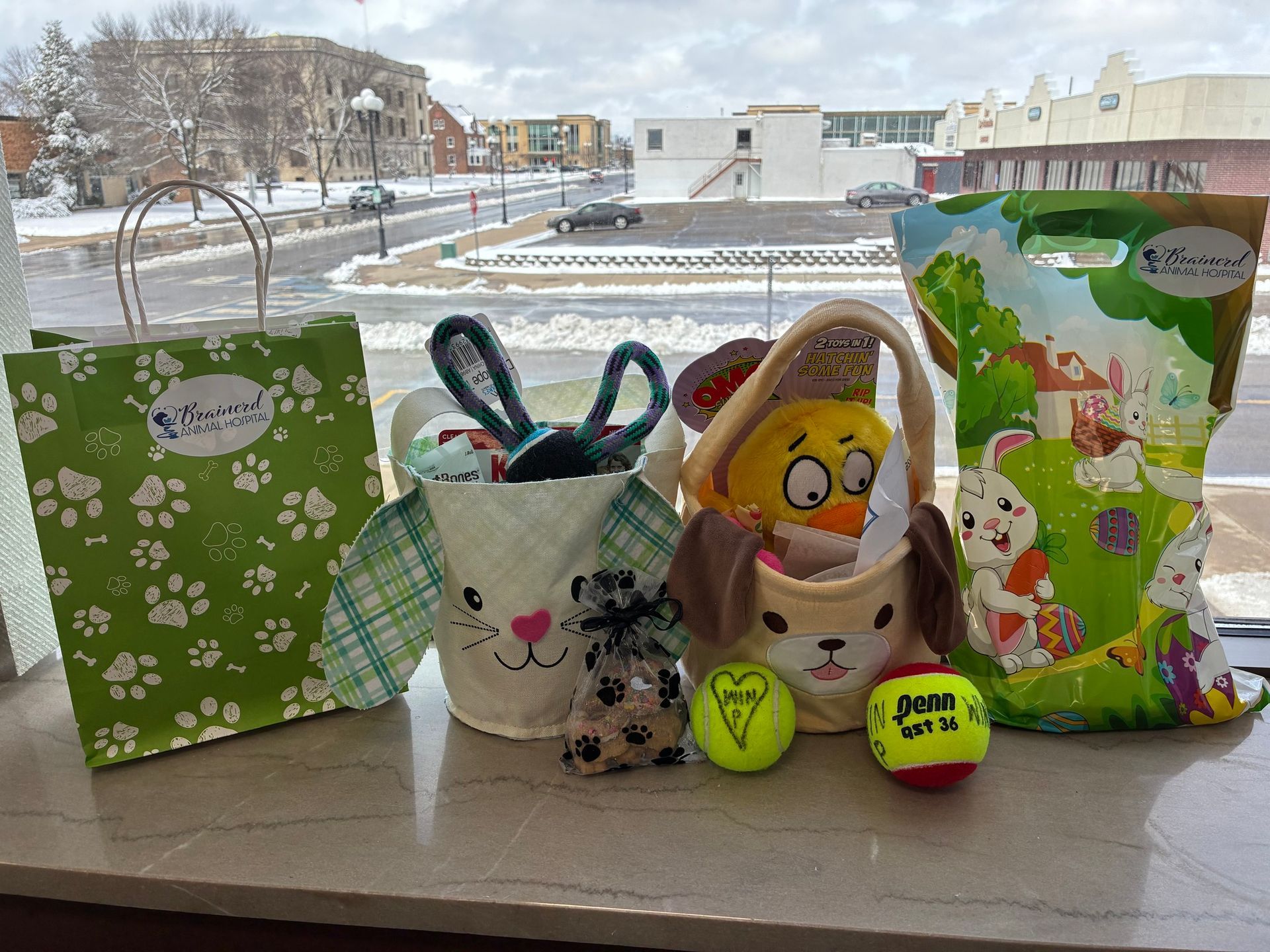 Easter display on a windowsill with pastel gift bags, bunny baskets, and decorated eggs in front of snowy buildings