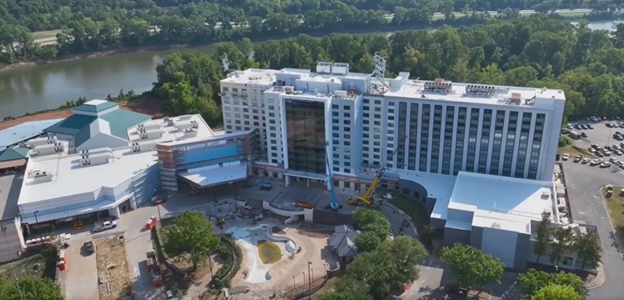 Aerial view of a tall white hotel building with a glass facade, located near a river and trees.