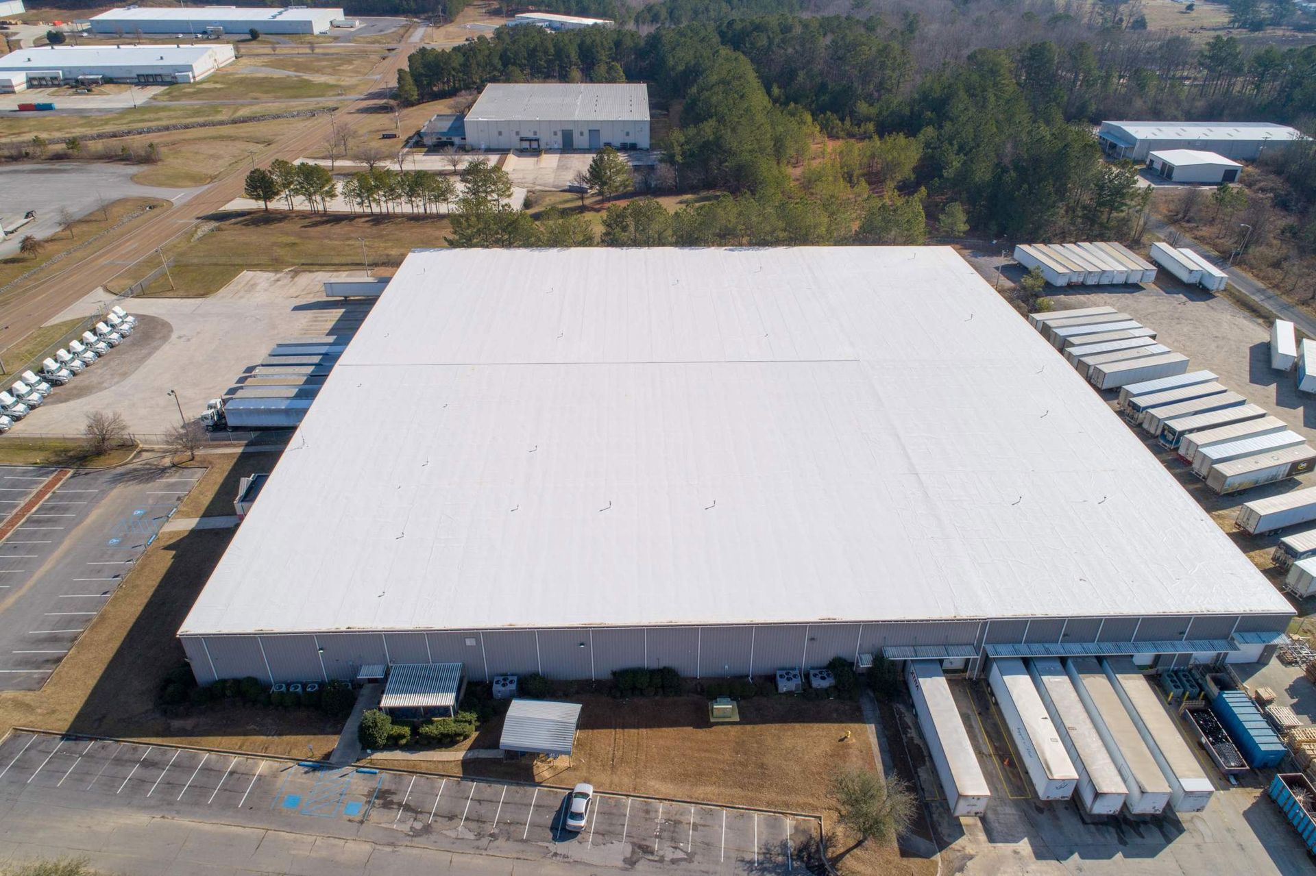 Aerial view of a large white warehouse with several loading docks, surrounded by trucks and a parking lot.