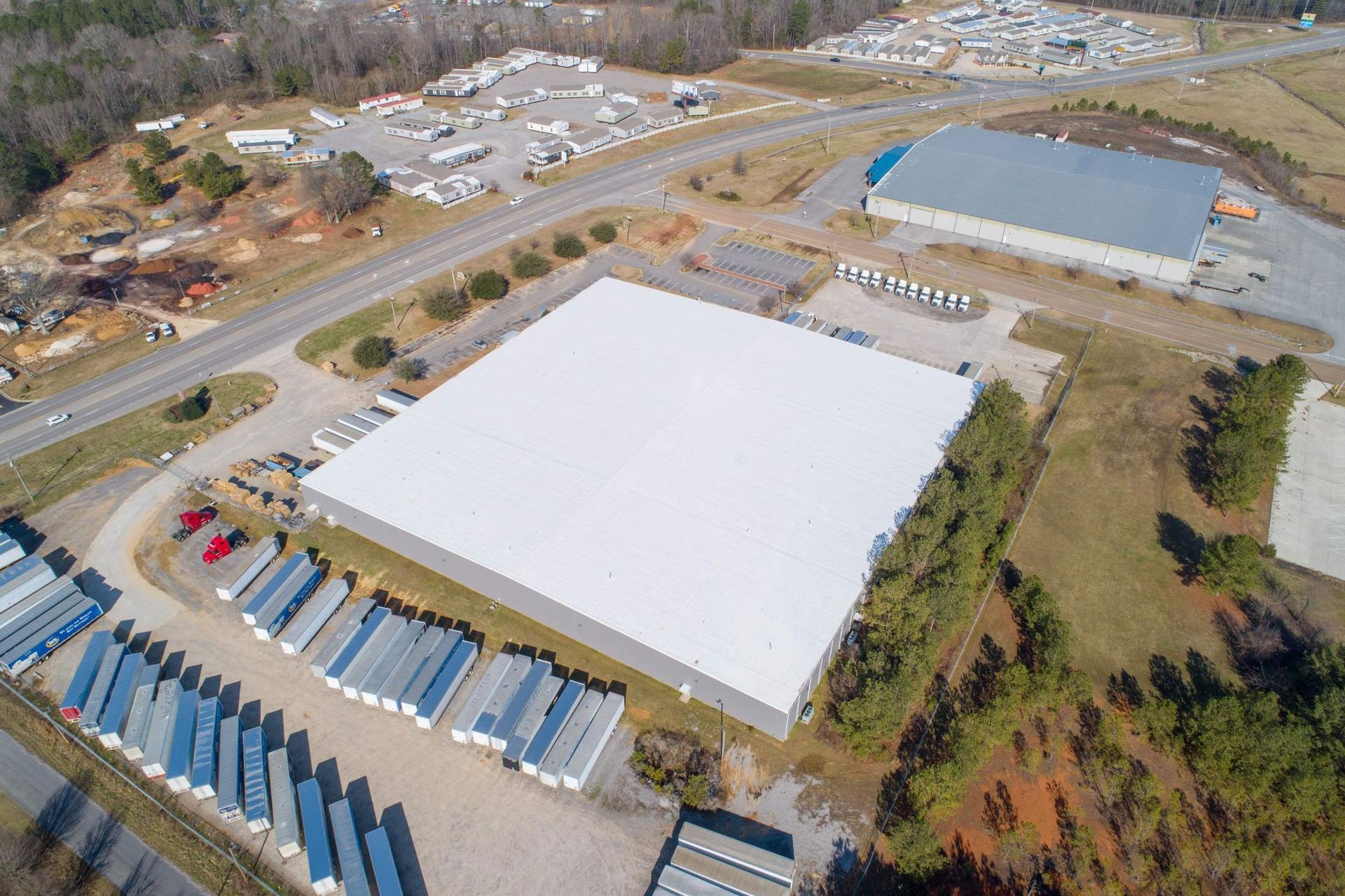 Aerial view of a large warehouse building with rows of trailers parked in front and other industrial buildings nearby.