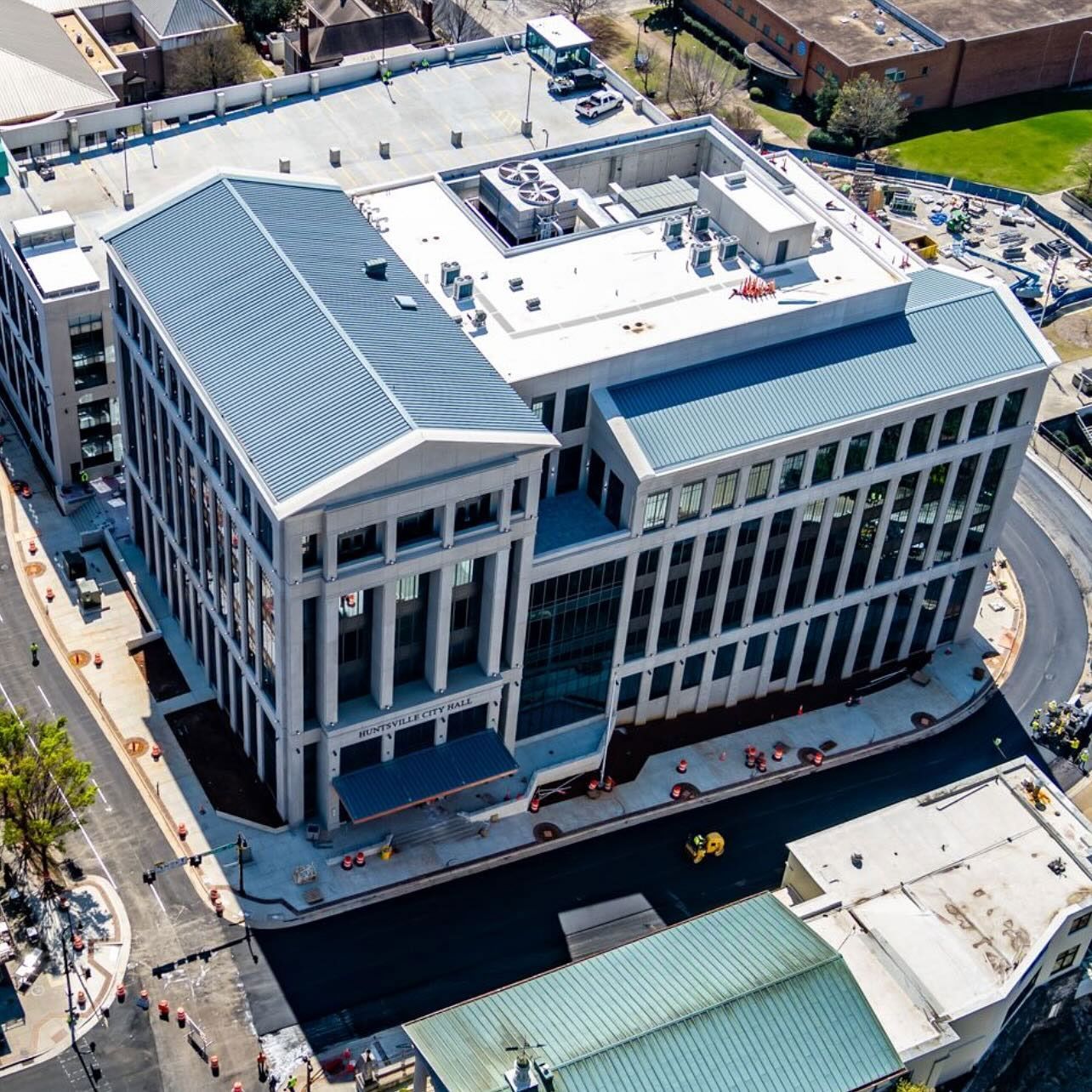 An aerial view of a light-colored building with a gray roof and columns in an urban area.