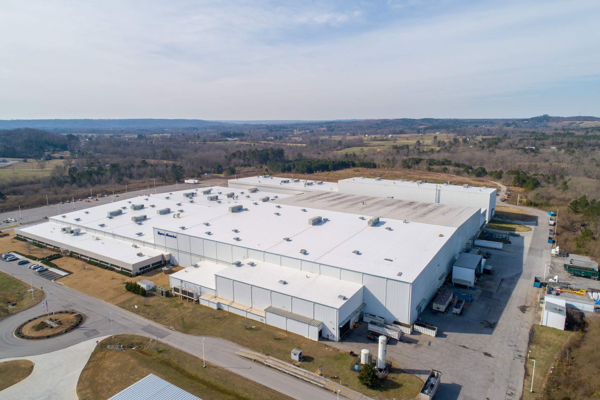 Aerial view of a large white industrial building with a flat roof and multiple loading docks, set in a rural area.