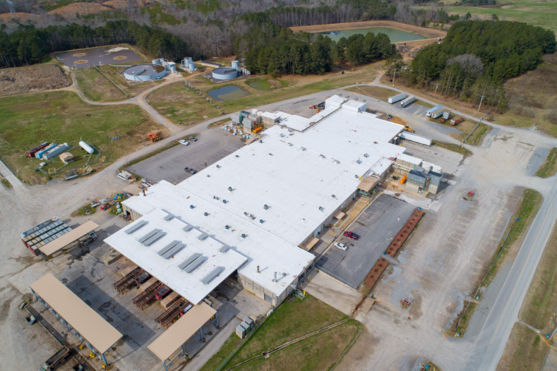 An aerial view of a large building with a white roof surrounded by trees.