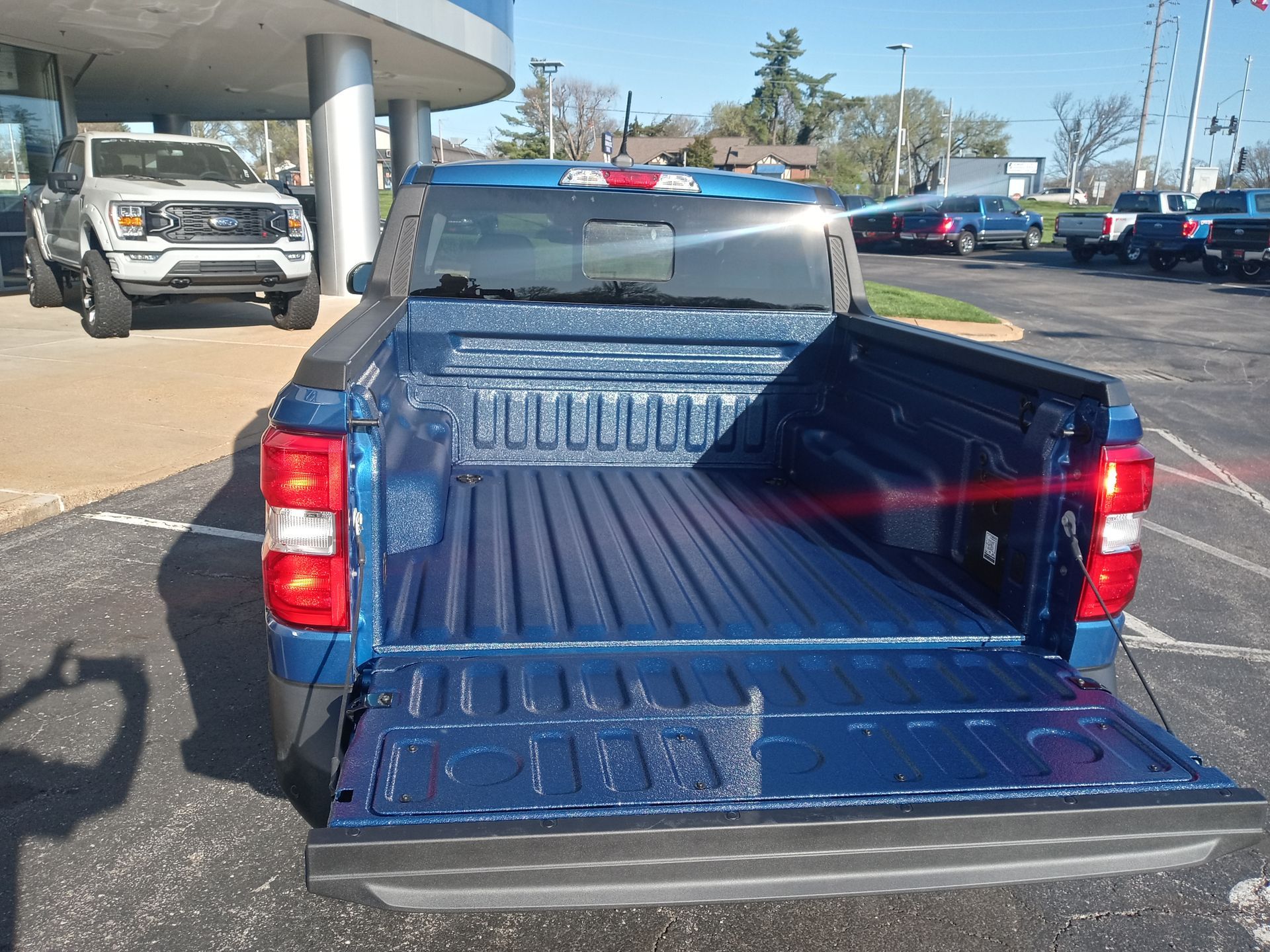 Blue pickup truck bed with open tailgate, parked outside a dealership.
