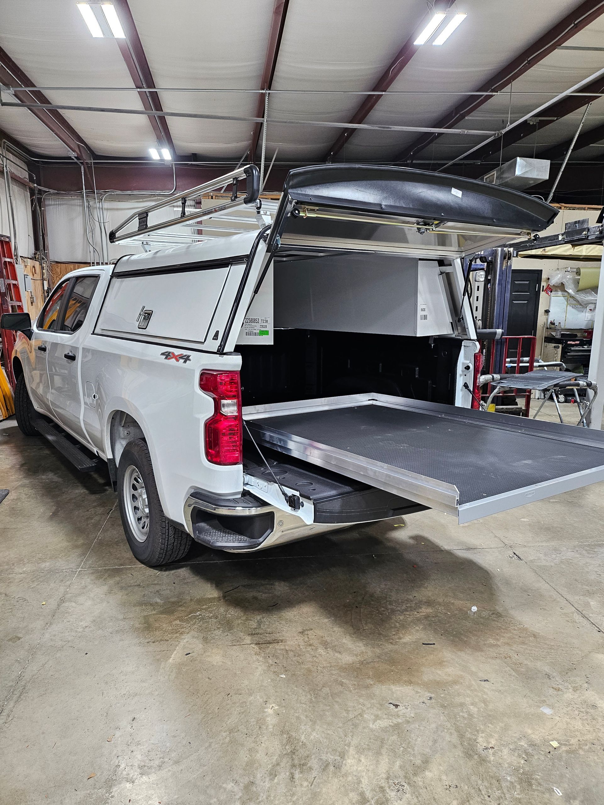 White truck with an open bed and a slide-out tray, inside a garage.