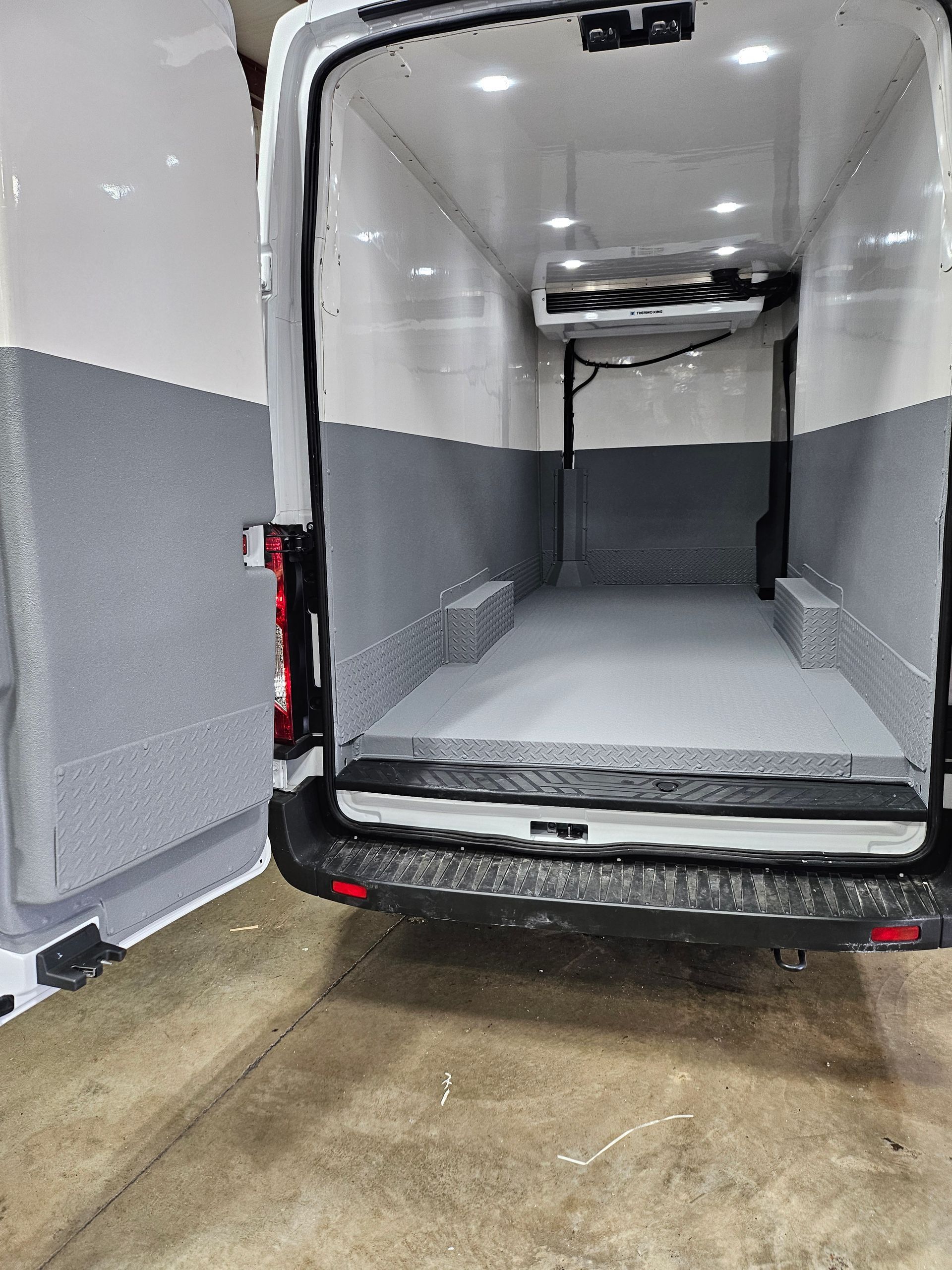 Interior of a refrigerated cargo van, gray and white insulated walls and floor. Rear doors open.