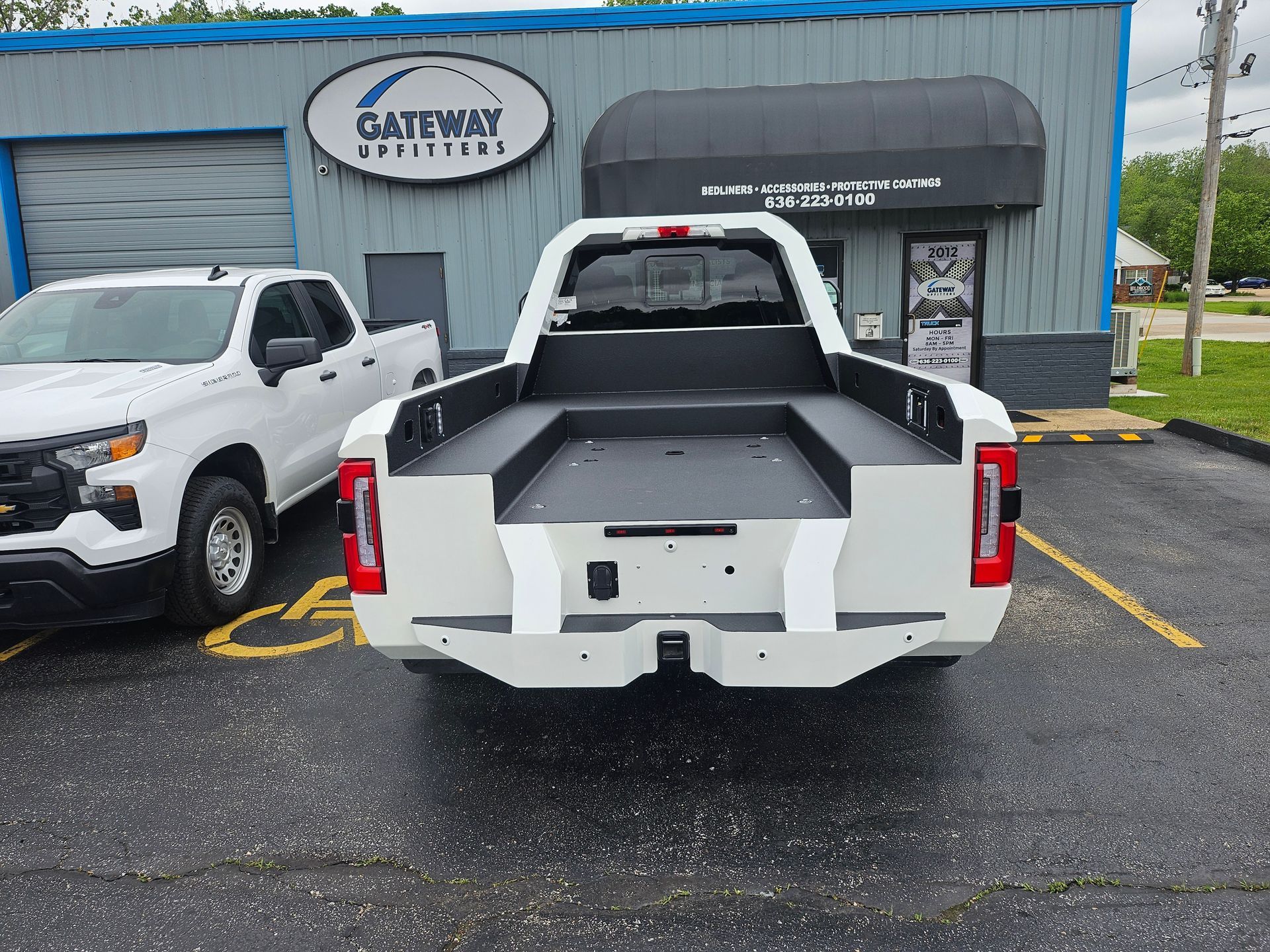 White truck with custom bed in front of a building with a business sign.