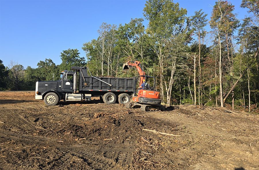 A dump truck is parked in a dirt field next to an excavator.