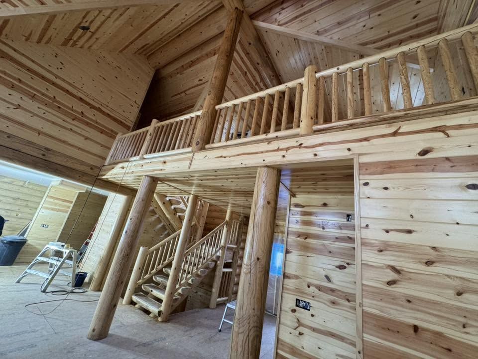 Wooden cabin interior with loft railing, staircase, and exposed pine walls and ceiling