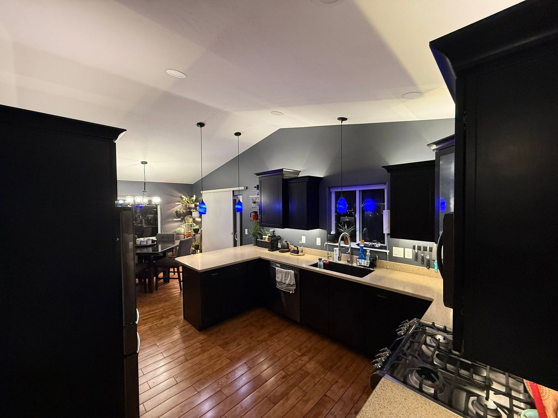 Modern kitchen with black cabinets, white countertops, and wood floors, viewed from the entryway