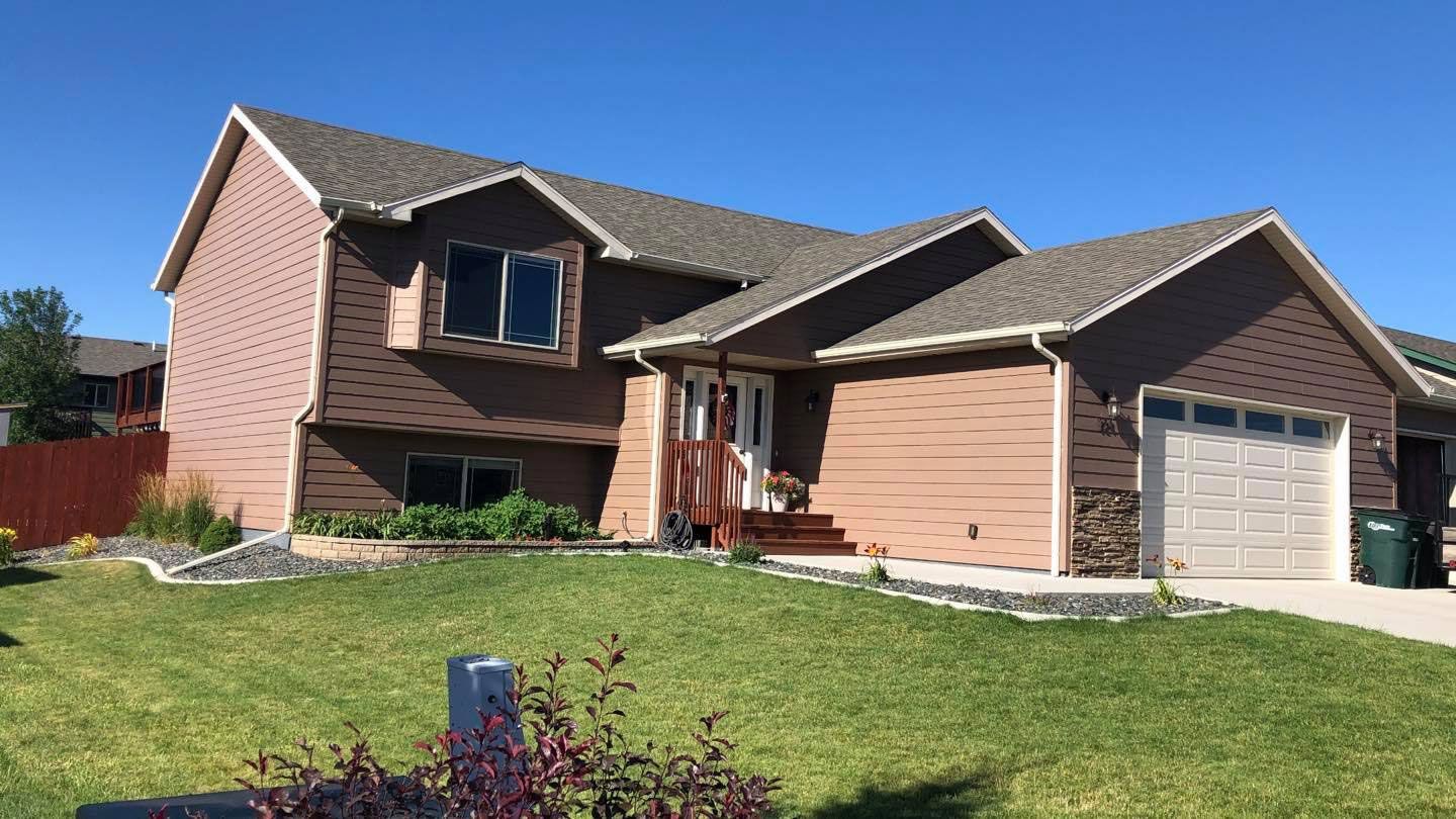 Two-story brown house with a green lawn and a sunny blue sky.