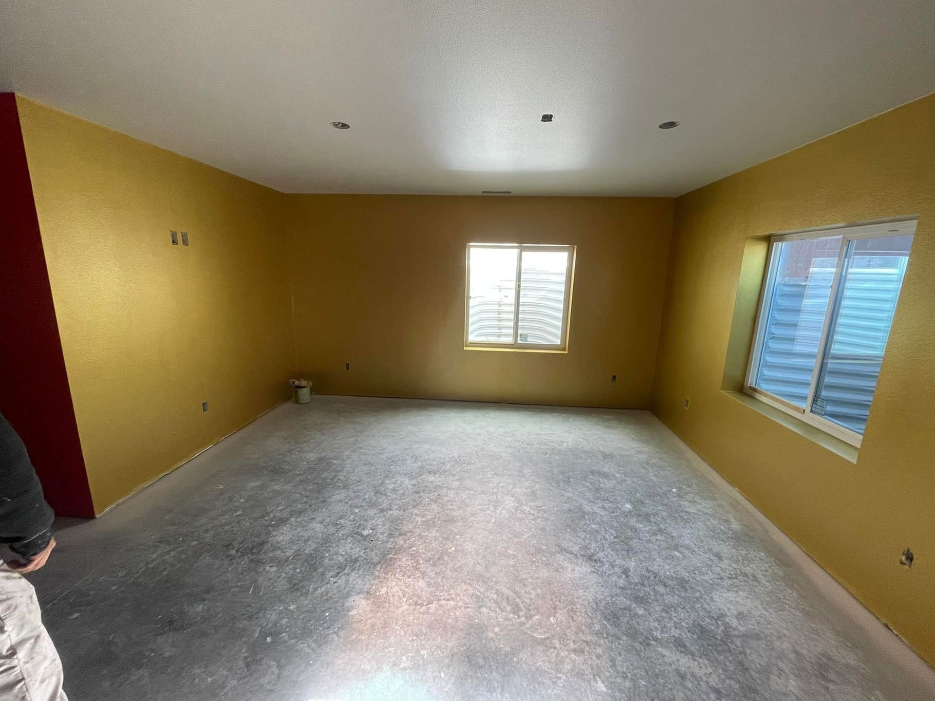 Empty room with gold walls, two windows with blue coverings, and concrete floor.