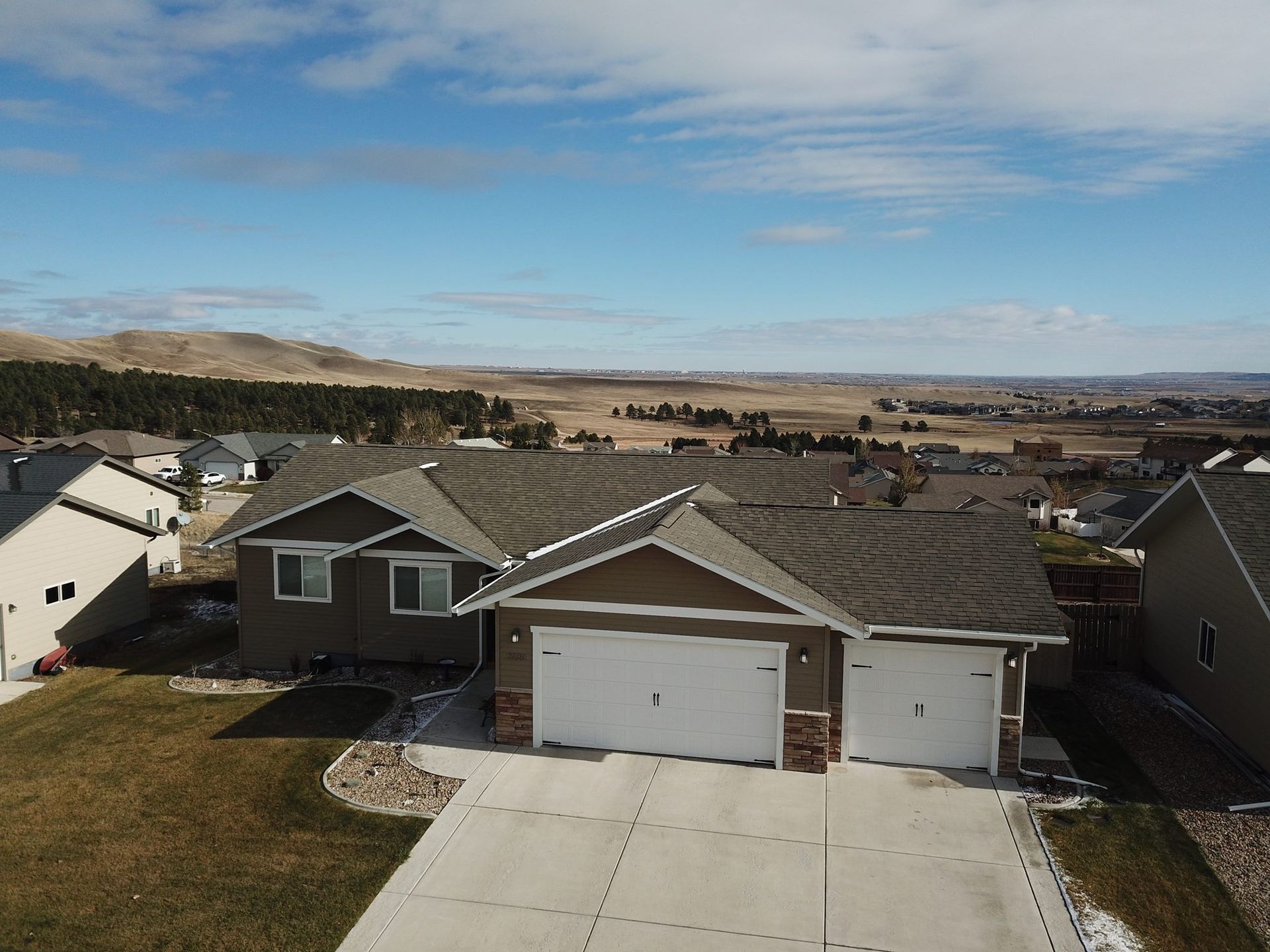 Brown house with white garage doors on a sunny day in a suburban neighborhood.